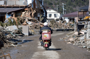2011年3月23日，一名邮递员骑车穿过宫城县东松岛市。沿海地区的道路正在修复。